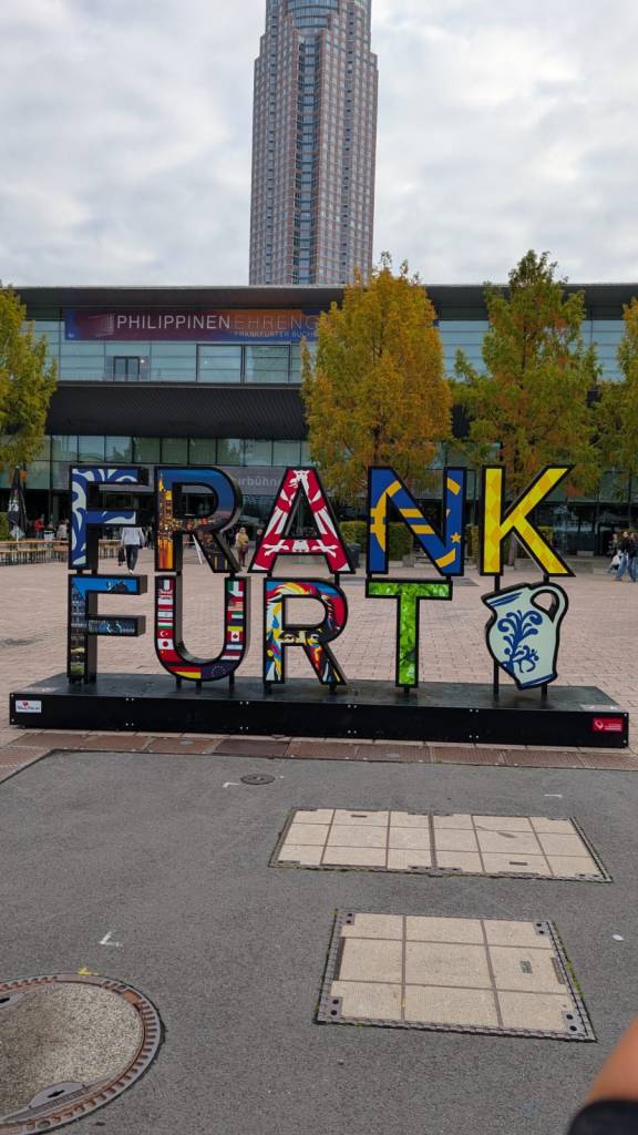 Colorful 'FRANKFURT' letters displayed outdoors, with a tall building in the background, showcasing a festive atmosphere.
