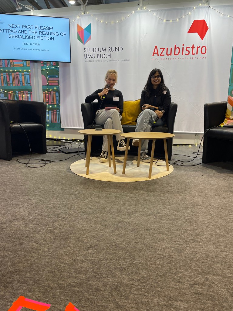 Two women seated on stage during a presentation at the Frankfurt Book Fair, discussing Wattpad and serialized fiction, with a screen displaying the topic and event details in the background.