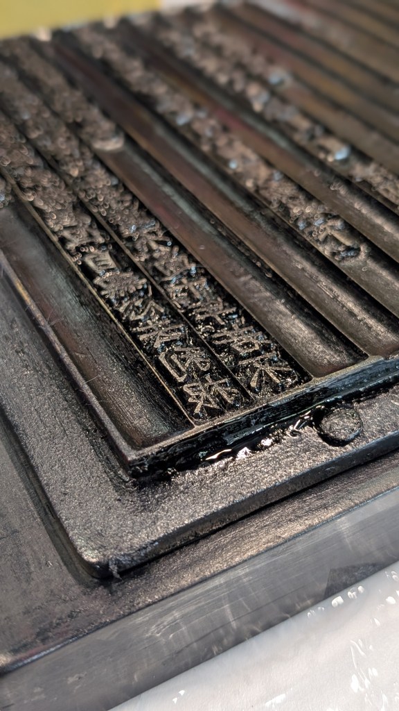 Close-up view of a black printing plate featuring Korean script used in early printing techniques.